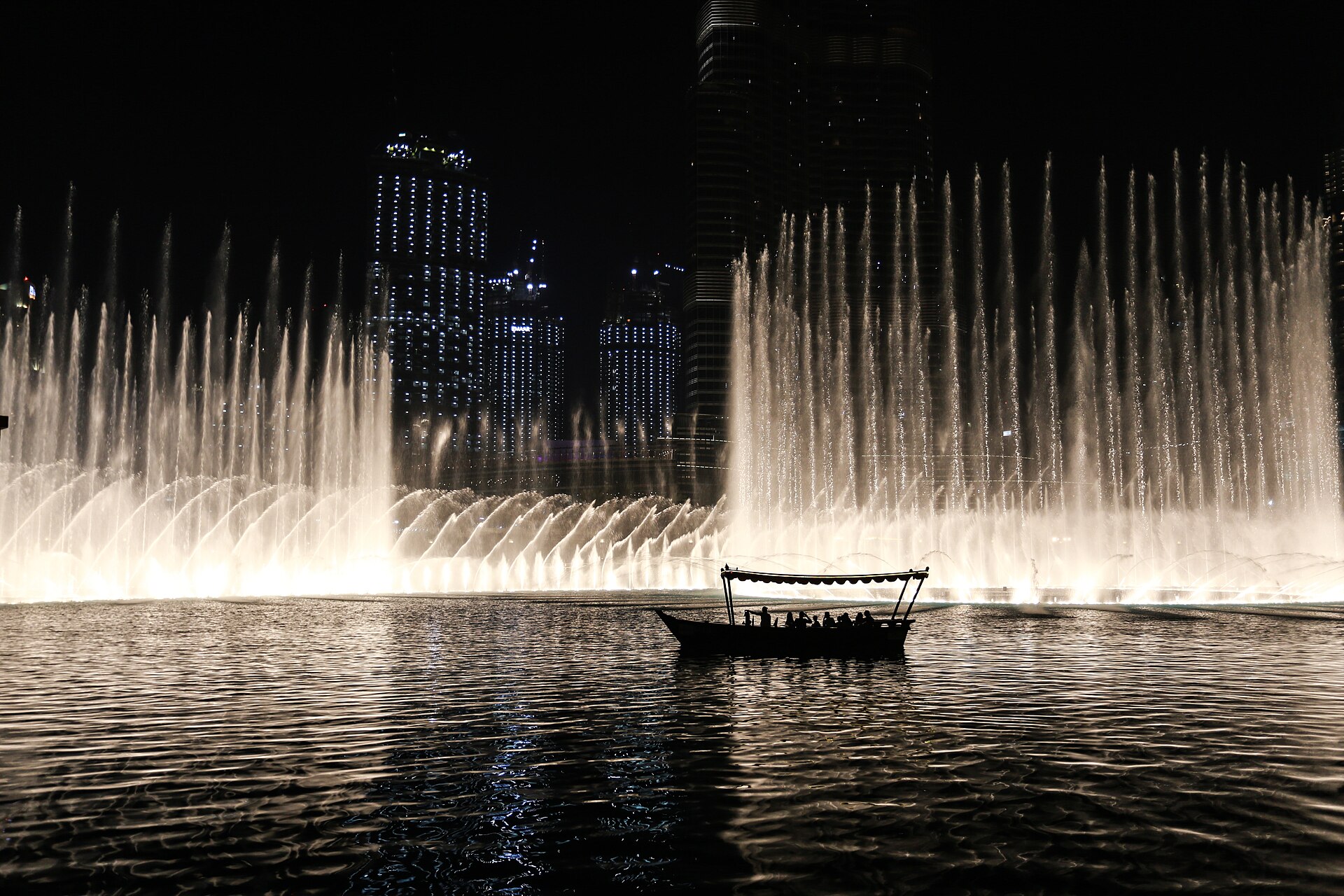 Jatos iluminados da Dubai Fountain e barco tradicional no lago à noite